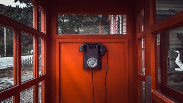 old-timey black telephone within a red phone booth